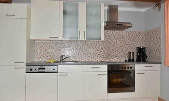 A modern kitchen with white cabinets and a countertop made of gray stone. In the background, a stove, a sink, and a kettle can be seen.