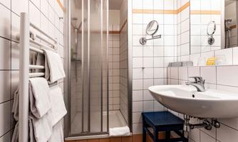 A modern bathroom with a shower area and a sink. Clean towels hang on the wall and a small blue table stands beside it.