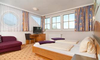 A cozy hotel room with two beds and a sofa. Large windows provide plenty of daylight and a pleasant atmosphere.