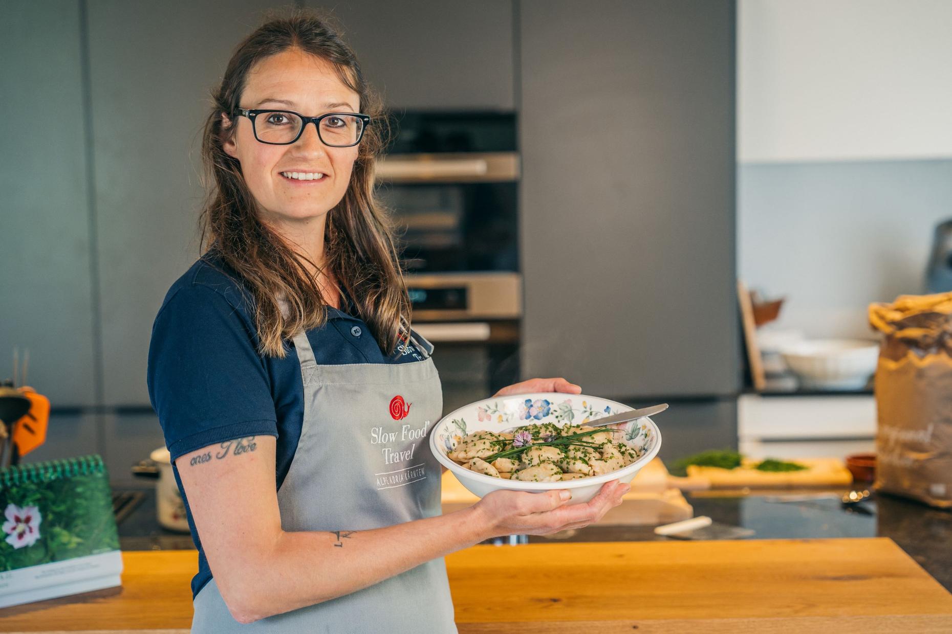 Frau mit Brille und Schürze hält Schüssel mit Gnocchi, Slow Food Travel AlpeAdria Kärnten