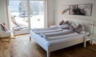 A modern bedroom with a large bed and appealing decor. Large windows provide a view of the winter landscape outside.