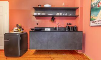 A modern kitchen with a black kitchen unit and a stylish refrigerator. The walls are painted in a soft pink.