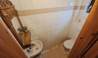 A small, bright bathroom with white tiles and wood details. It includes a bidet, a toilet, and a window for daylight.