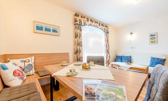 A cozy interior with a wooden table and a bench. The decor is bright and friendly, with colorful curtains and decorations.