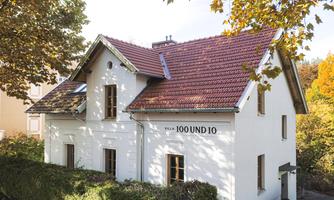 A charming white house with a red tiled roof. Surrounded by colorful trees in autumn.