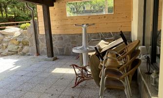 A covered outdoor area with stacked chairs and a table. The floor is paved with stones and there is a view of a stone wall.