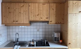 A modern kitchen with wooden cabinets and a stainless steel sink. On the stove are a pot and a coffee machine.