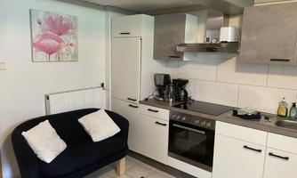 A modern kitchen with a black sofa and a refrigerator. A decorative picture with pink flowers is hanging on the wall.