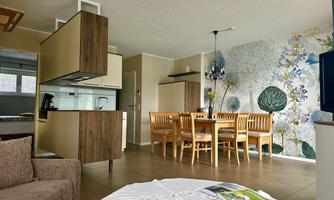 A modern living area with an open kitchen and a dining area. The walls are decorated with a floral wallpaper and the room is bright and inviting.