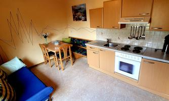 A small, cozy kitchen with a dining table and chairs. The walls are painted in warm colors, and there is a couch with colorful cushions.