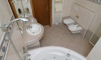 A modern bathroom with a bathtub, a sink, and a bidet. The walls are brightly tiled and there are large mirrors.