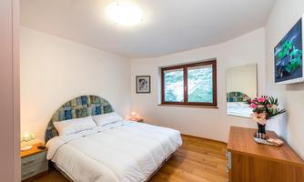 A modern bedroom with a large double bed and warm wooden floors. The room has a window overlooking greenery and a stylish decor.