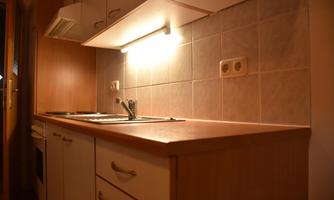 A modern kitchen with wooden cabinets and a functional work surface. The lighting creates a pleasant atmosphere.