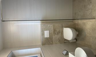A modern bathroom with a shower and a toilet. The walls are brightly tiled and there is a window for natural light.