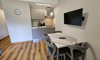 A modern kitchen unit with a dining table and chairs. A television hangs on the wall, and the room has a bright, inviting style.