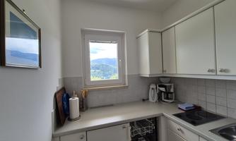 A bright kitchen with white cabinets and a window overlooking the landscape. On the countertop, there are some kitchen appliances and utensils.