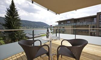 An elegant balcony with two chairs and a table. In the background, there is a beautiful view of a lake and the surrounding mountains.