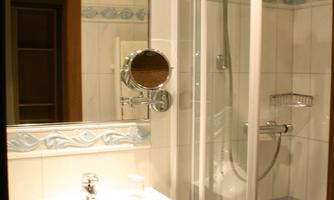 A modern bathroom with a transparent shower and a sink. The wall tiles are light and have a subtle pattern.