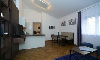A modern apartment with a cozy dining area and an open kitchen. There are bright curtains and a wooden floor that gives the room a warm atmosphere.