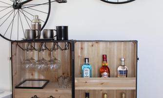 A stylish wooden bar shelf with various spirits and glasses. Above it hangs a decorative bicycle that adds a modern touch to the room.