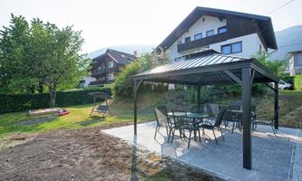 A beautiful garden with a covered dining area and modern furniture. In the background, several houses and trees can be seen.