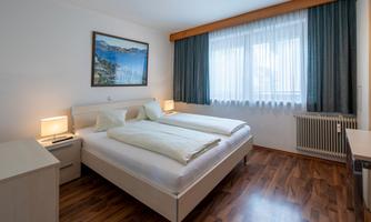 A cozy bedroom with two single beds and a large window. A picture of a coastal landscape hangs on the wall.