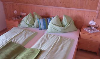 A cozy bedroom with a double bed and green pillows. On the nightstand, there is a lamp and a small cloth.