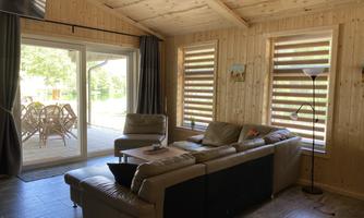 A cozy living room with wood paneling and modern furniture. Large windows provide a view of the outdoor area with a dining space.