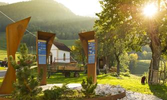 An informative site in nature with metal panels and a small building in the background. The scenery is framed by gentle hills and warm sunlight.