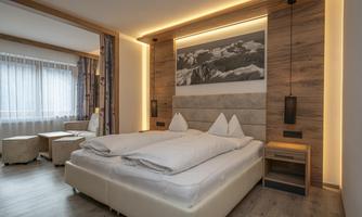 A modern bedroom with a large bed and a cozy seating area. The warm lighting and wood paneling create an inviting atmosphere.