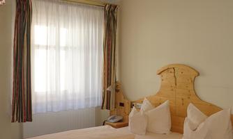 A cozy bedroom with two beds and wooden furniture. Large windows provide plenty of daylight.