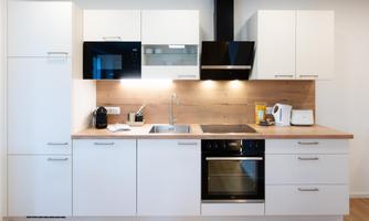 A modern kitchen with white cabinets and wooden details. It is equipped with a stove, a sink, and various kitchen appliances.