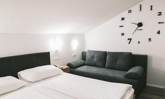 A modern bedroom with a double bed and a gray sofa. There is a large wall clock on the wall.