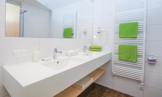 A modern bathroom with bright tiles and a large sink. Green towels and a towel rack add a fresh touch to the space.