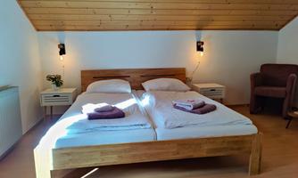 A cozy bedroom with a wooden bed and two mattresses. The room has slanted walls and warm lighting.