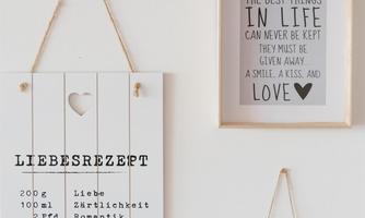 On a wall hang two pictures. The left picture shows a "recipe for love" with ingredients, the right one a quote about the best things in life.