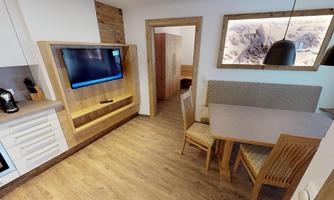 A modern living kitchen with a wood look and a television on the wall. The dining area consists of a table and chairs.