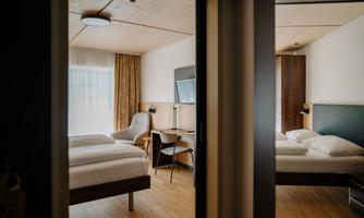 A modern hotel room with two beds and natural light. There is a desk, a television, and a pleasant atmosphere.