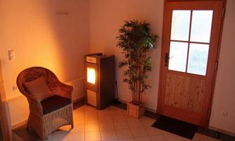 A cozy entrance area with a rattan chair, a heating unit, and a plant. The door to the outdoor area has several windows and provides bright light.