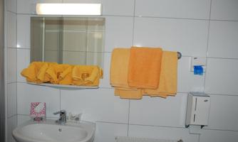A bathroom with a sink, a mirror, and several yellow towels. Soap dispensers and a towel rack are mounted on the wall.