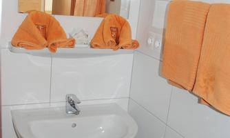 A bathroom with white tiles and a sink. Two orange towels hang decoratively on the towel rack.