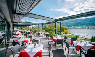 A modern restaurant with tablecloths in red and white. The view of the lake and the mountains in the background creates an inviting atmosphere.