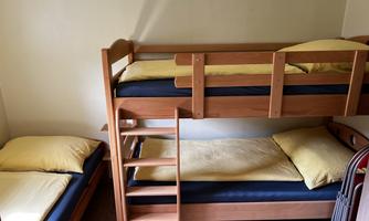 A simple room with a wooden bunk bed. On the right is a single bed with yellow bed sheets.
