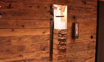 A rustic entryway with a wooden wall. The bench is decorated with a checked blanket and there is a large mirror.