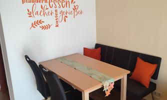 A cozy dining area with a table and a bench. A decorative saying is on the wall.