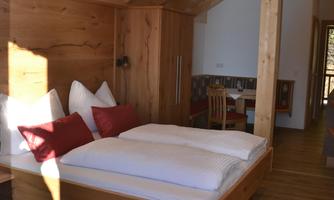 A modern wooden room with a double bed and red cushions. The ceiling is high and creates a cozy atmosphere.