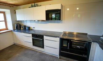 A modern kitchen with white cabinets and a large window. The countertop is made of gray stone and there are various kitchen appliances.