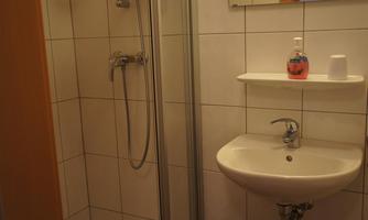 A small bathroom with a shower and a sink. The walls are tiled with white tiles.