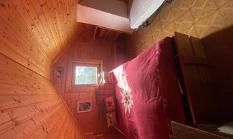 A cozy bedroom with wood paneling and a large window. The bed is decorated with red bedding and pillows.