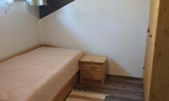A simple room with a single bed, a nightstand, and a wardrobe. The walls are painted in light white and the floor is made of wood.